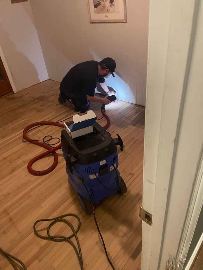 A man is working on a wooden floor with a vacuum cleaner.