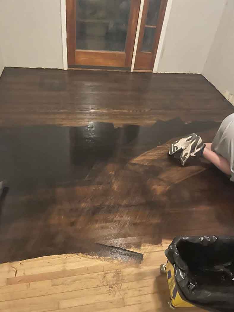 A person is painting a wooden floor in a room.