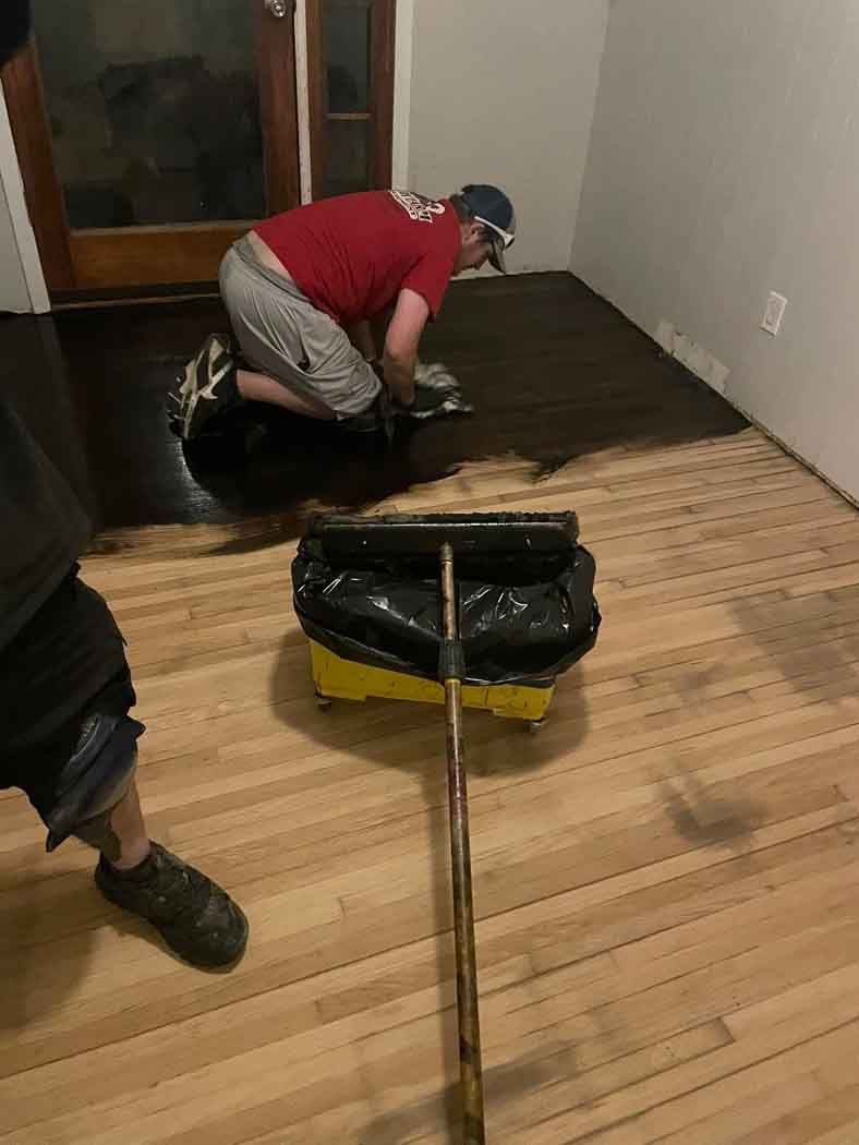 A man is painting a wooden floor with a roller.