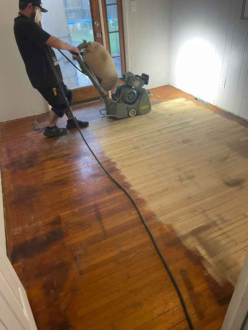 A man is sanding a wooden floor with a machine.
