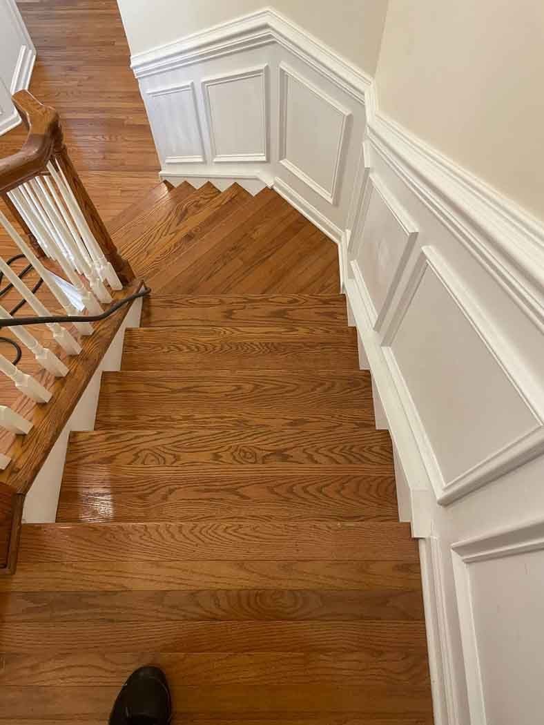 A person is standing on a wooden staircase in a house.