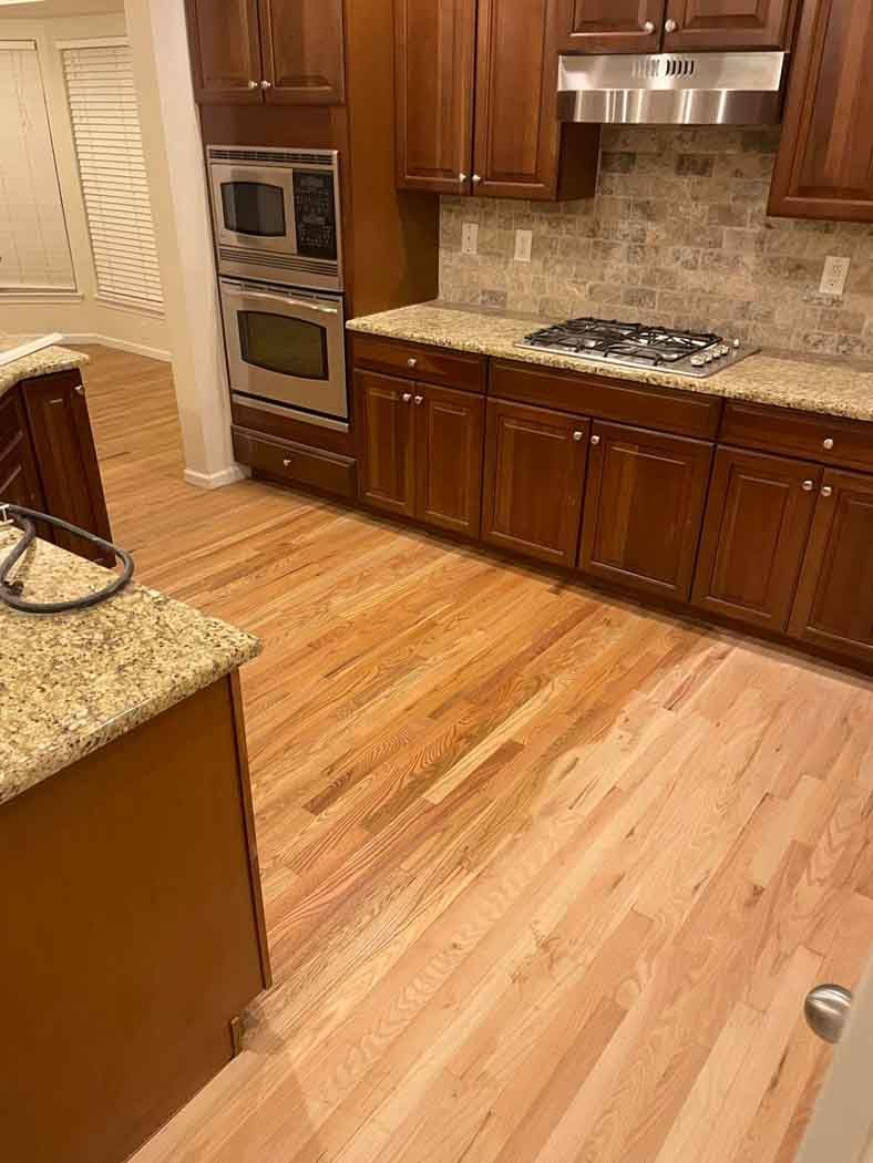 A kitchen with hardwood floors , stainless steel appliances , granite counter tops , and wooden cabinets.
