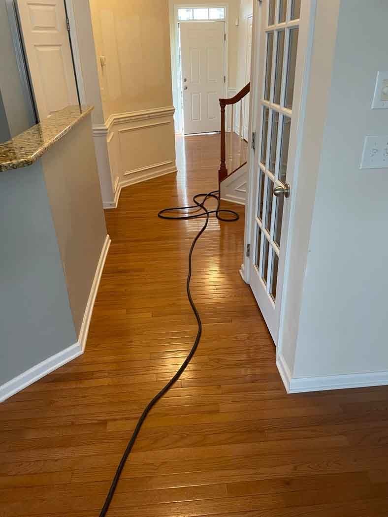 A hallway with hardwood floors and a black cord hanging from the ceiling.