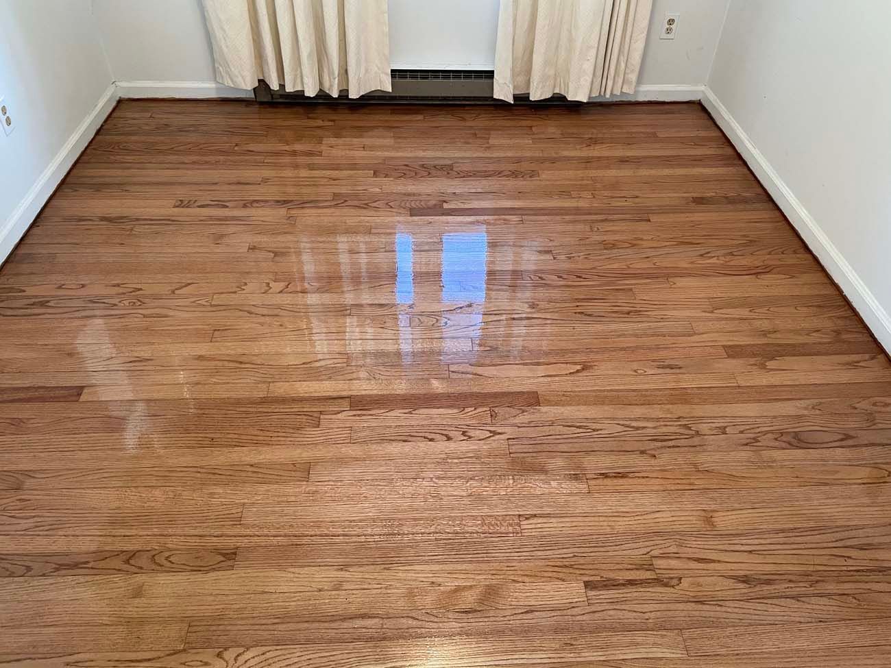 A bedroom with hardwood floors and white curtains.