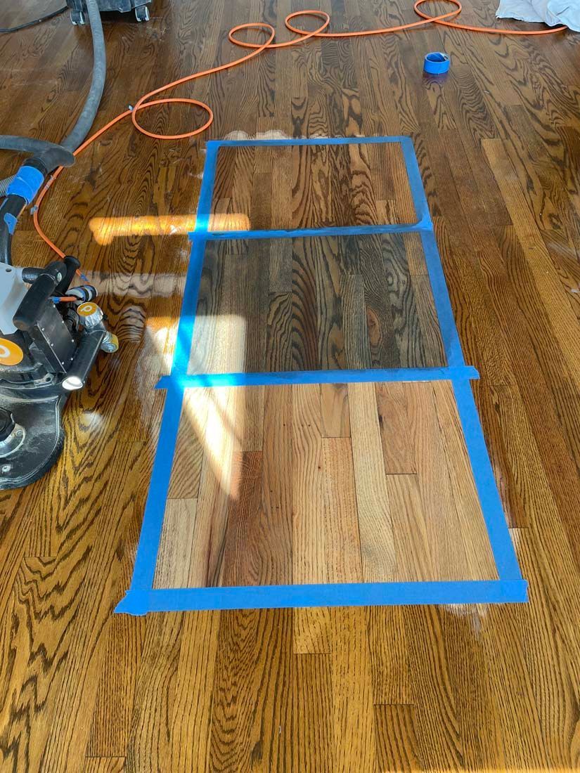 A wooden floor with blue tape on it and a vacuum cleaner.