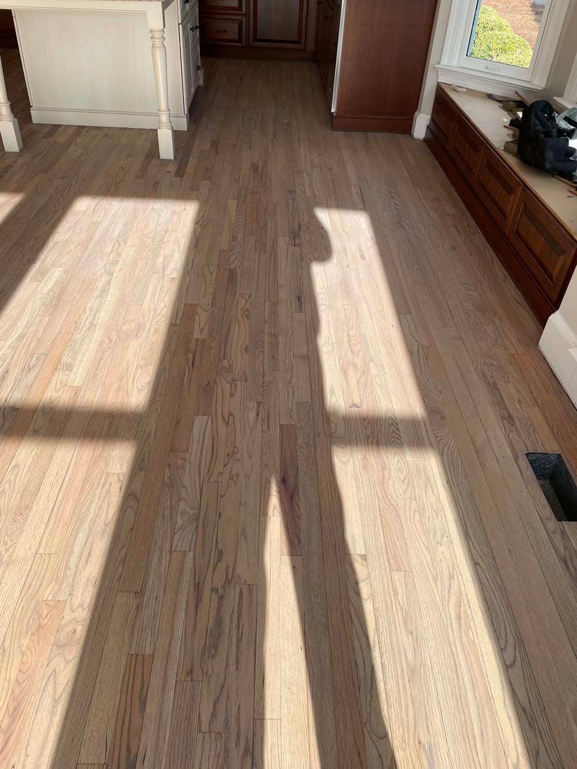 A wooden floor in a kitchen with a shadow of a person on it.
