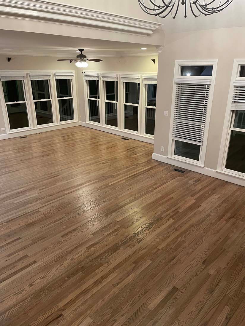 An empty living room with hardwood floors and lots of windows.