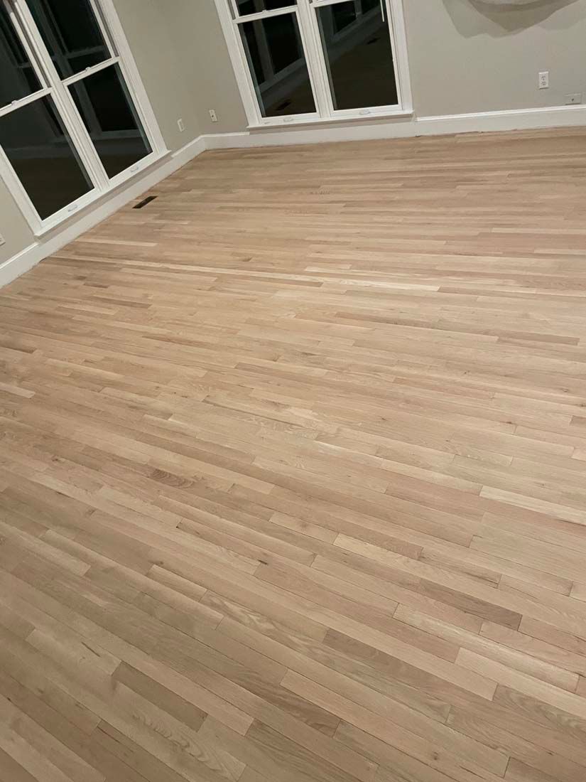 A living room with a wooden floor and two windows.