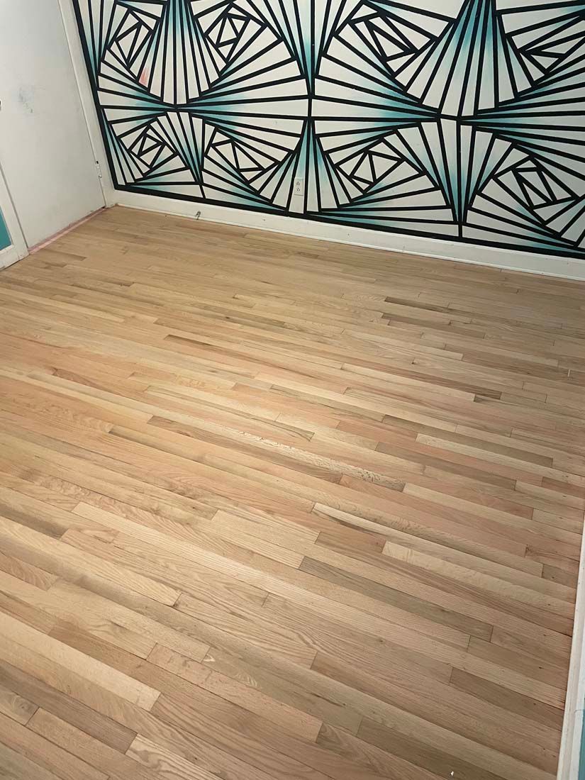 A wooden floor in a room with a geometric design on the wall.
