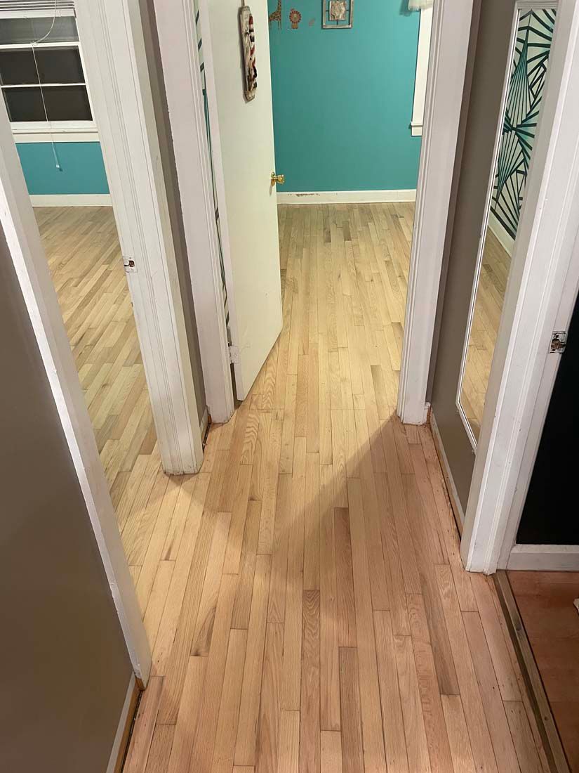 A hallway with hardwood floors between two rooms in a house.