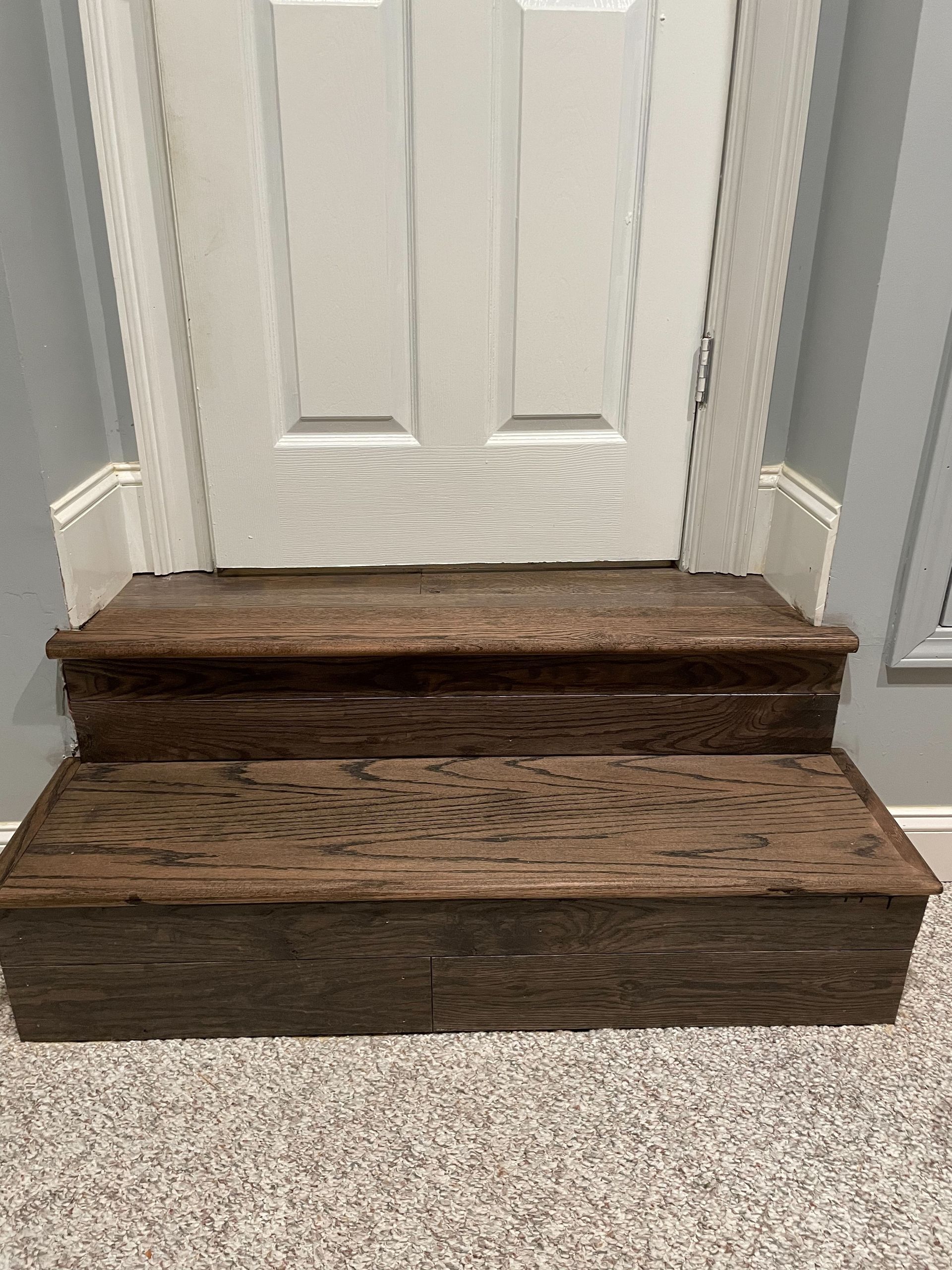 A set of wooden stairs leading up to a door in a room.