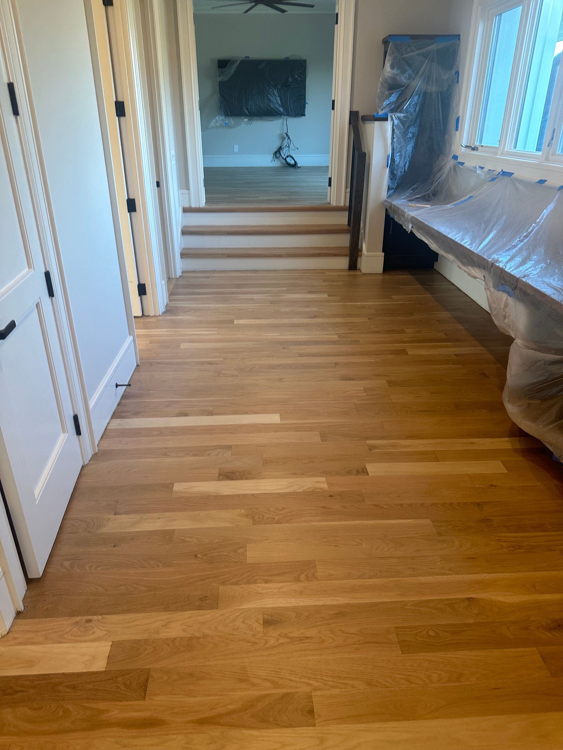 A hallway with hardwood floors and stairs leading to a living room.