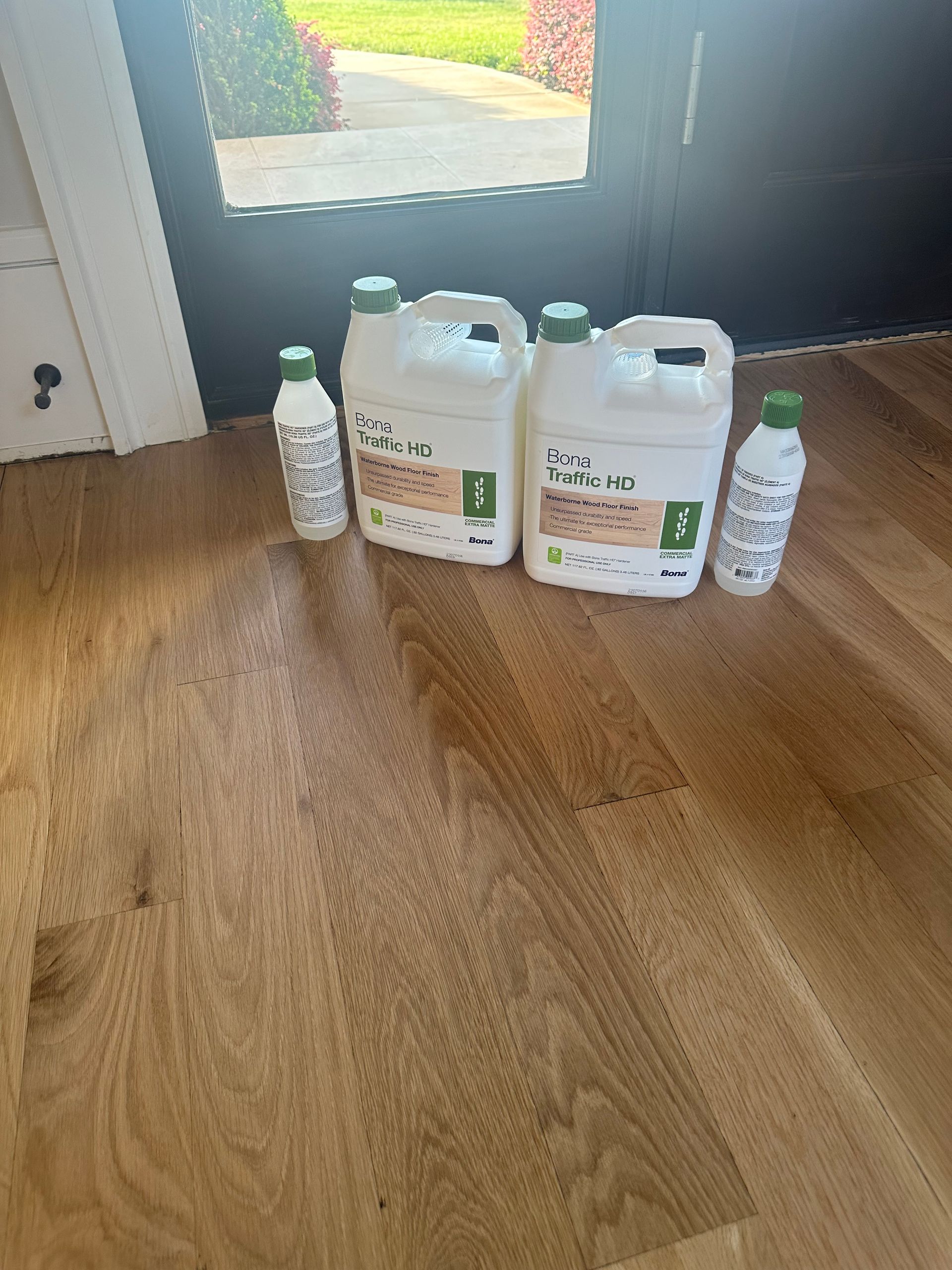 Three bottles of liquid are sitting on a wooden floor.