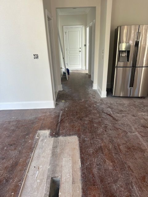 A hallway with a stainless steel refrigerator and a hole in the floor.