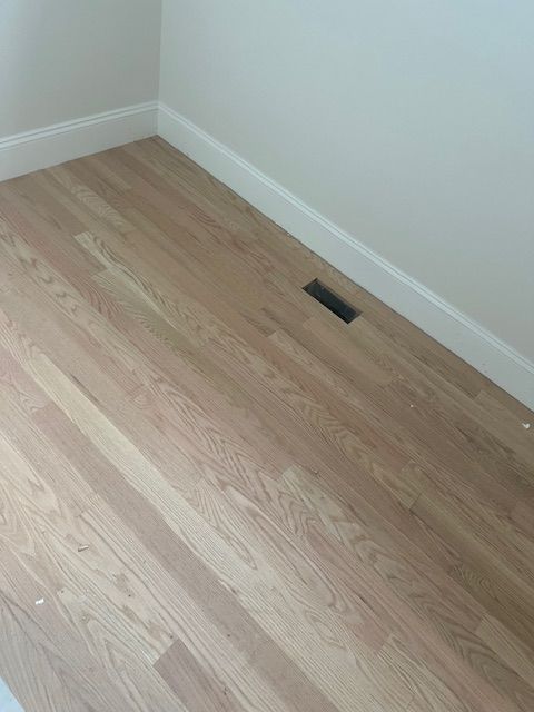 A wooden floor with a vent in the corner of a room.