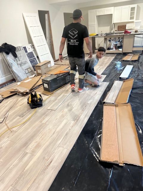 Two men are installing a wooden floor in a kitchen.
