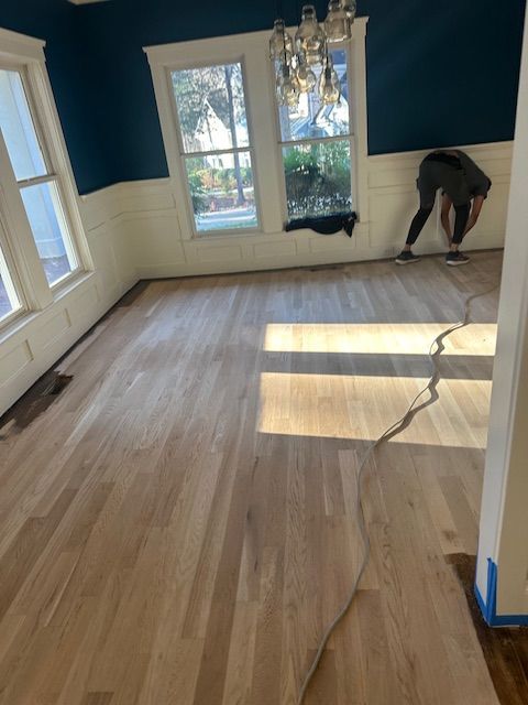 A person is painting a wooden floor in a room with blue walls.