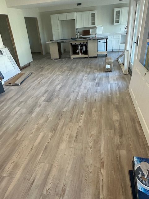 A living room with hardwood floors and a kitchen in the background.