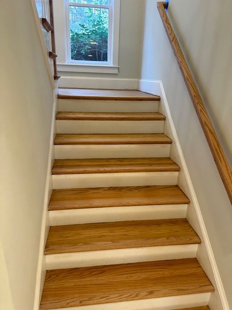 A set of wooden stairs with a white railing and a window.