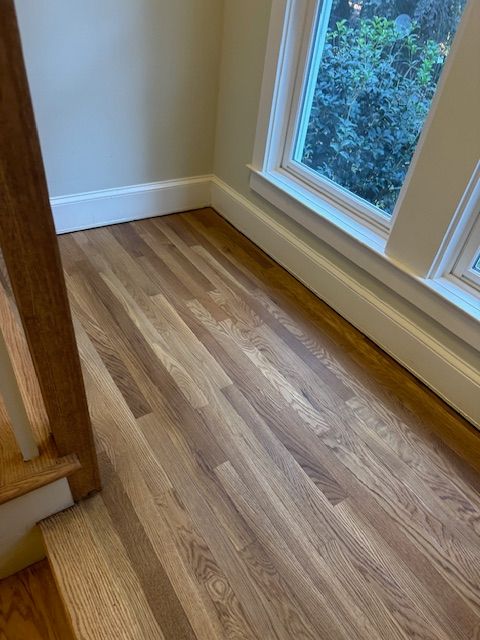 A wooden floor in a room next to a window.