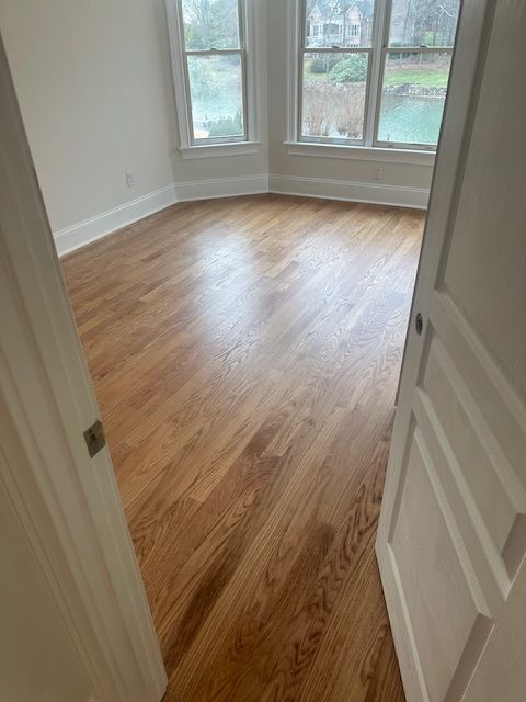 An empty room with hardwood floors and two windows.