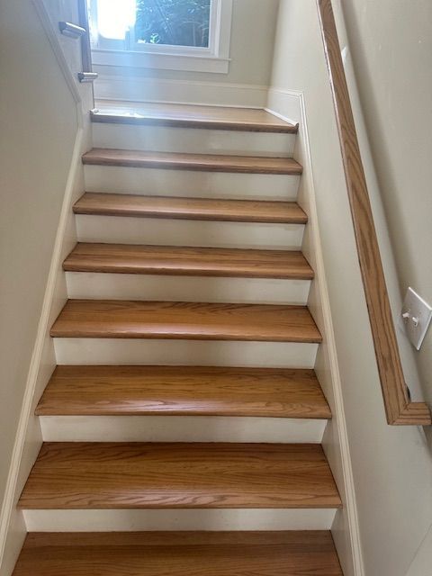 A set of wooden stairs with white walls and a wooden railing.