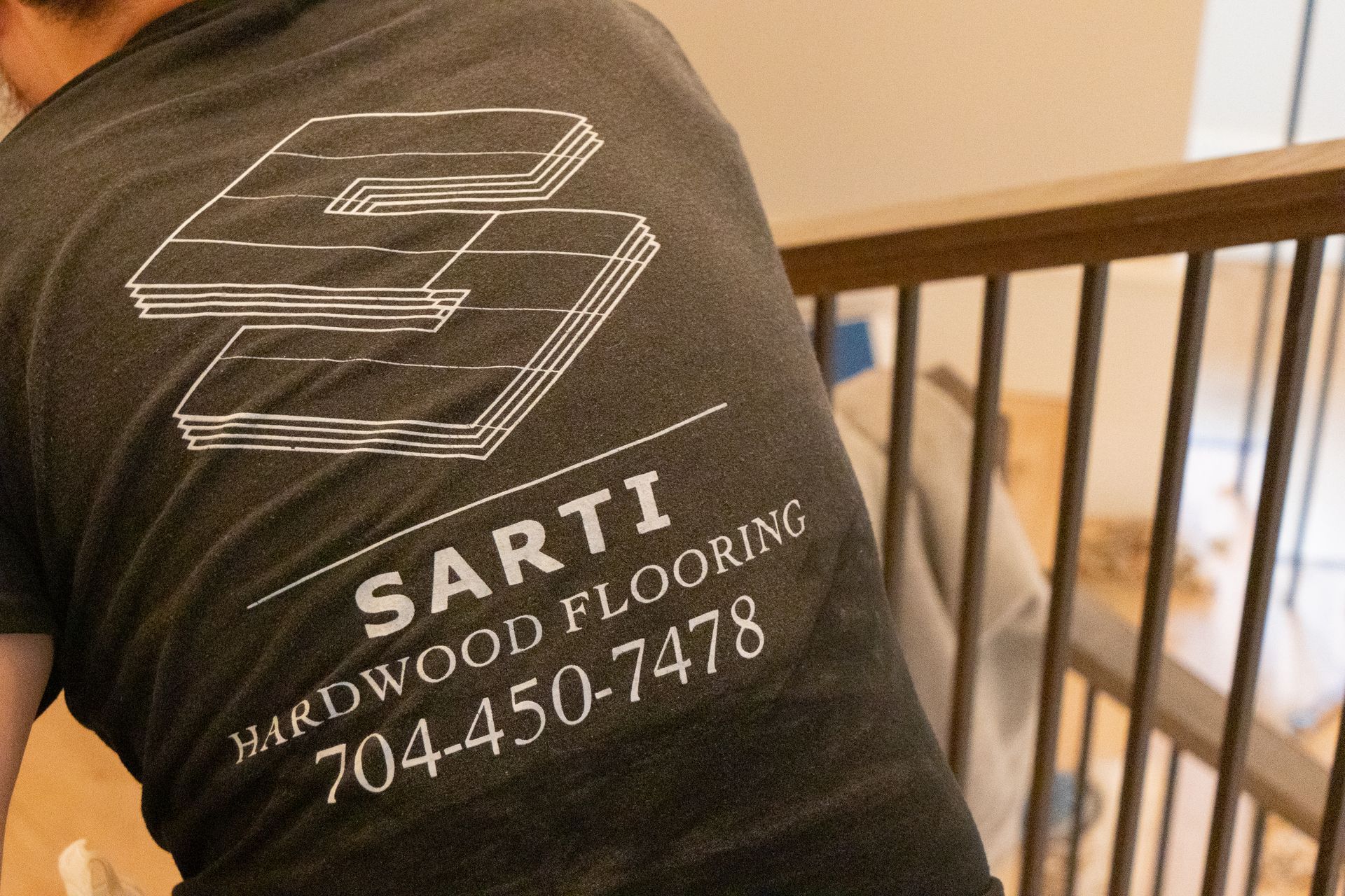 A man wearing a shirt that says sarti hardwood flooring is standing on a staircase.