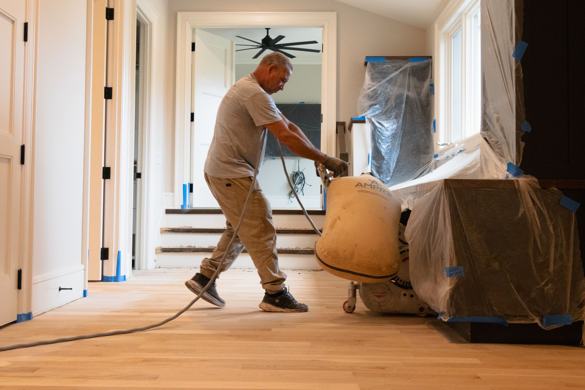 A man is sanding a wooden floor in a living room.