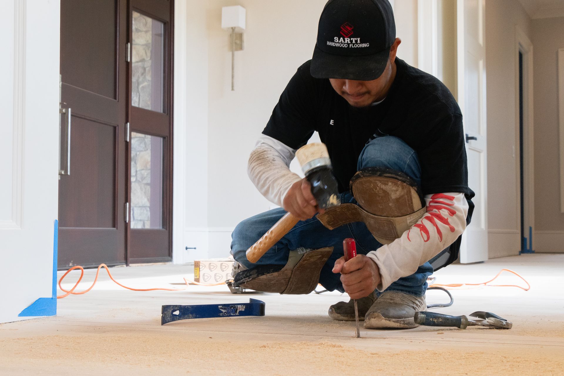 A man is kneeling on the floor using a hammer and a screwdriver.
