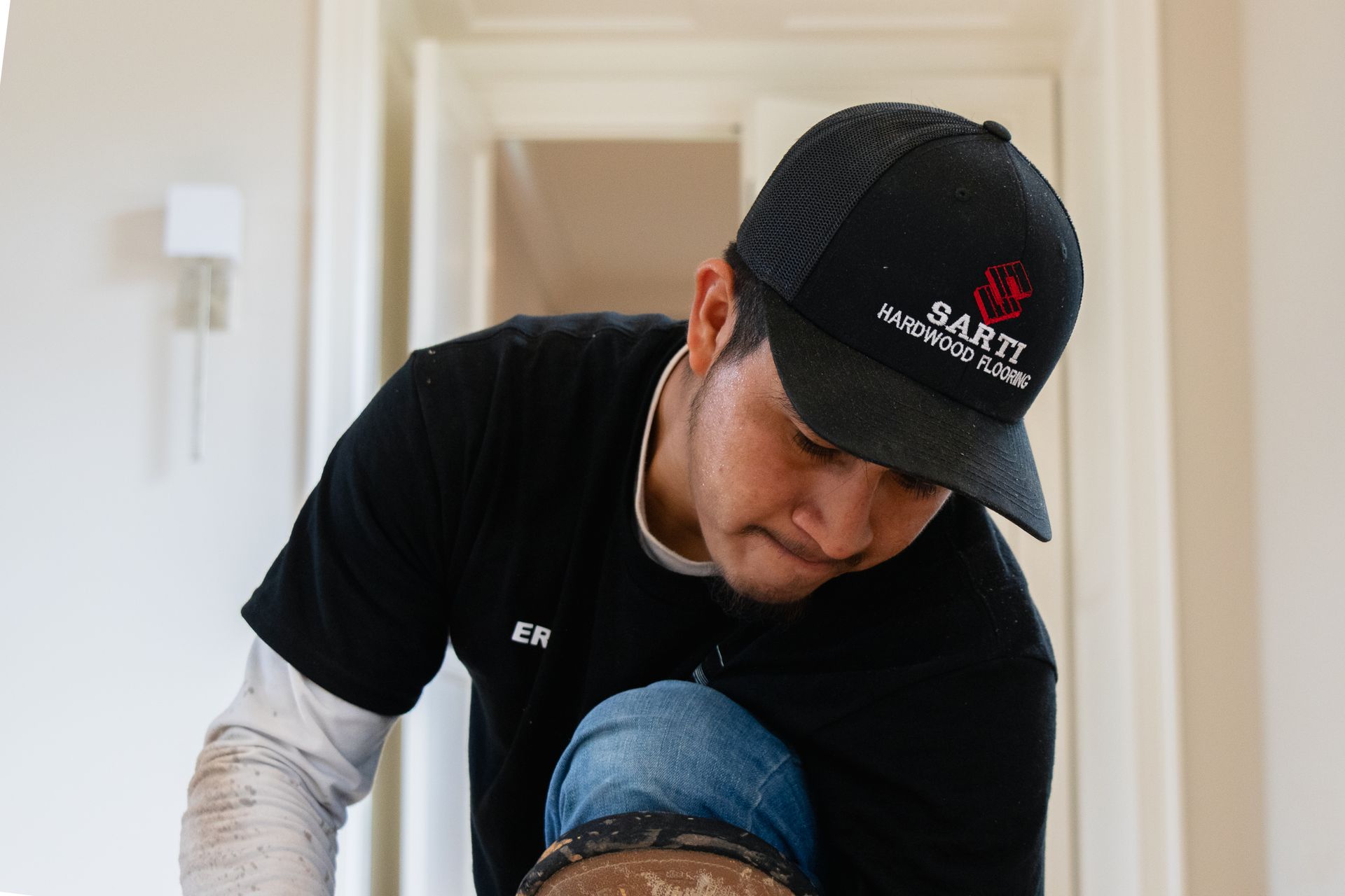 A man wearing a black hat is working on a wooden floor.