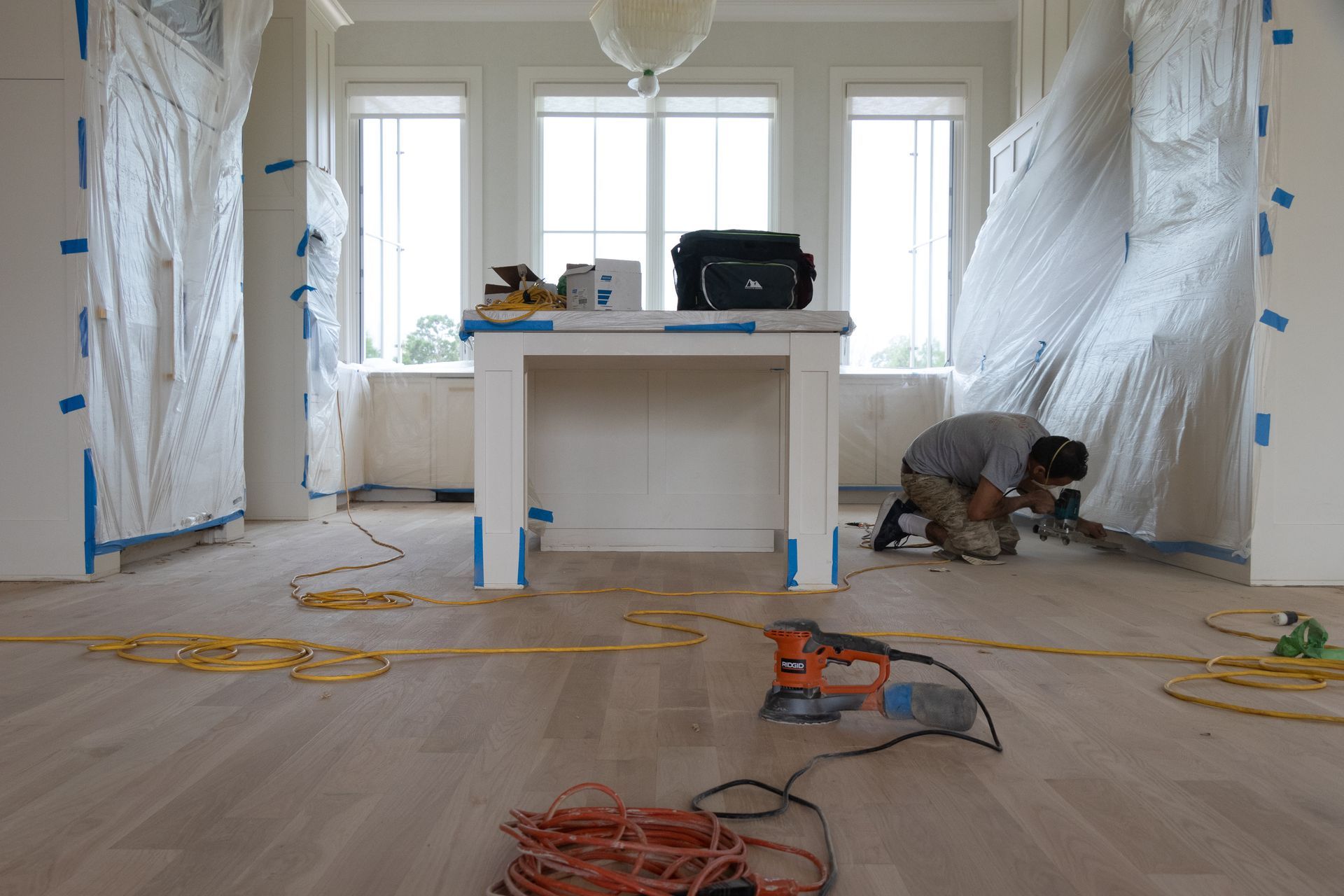 A man is kneeling down in a room with a drill on the floor.