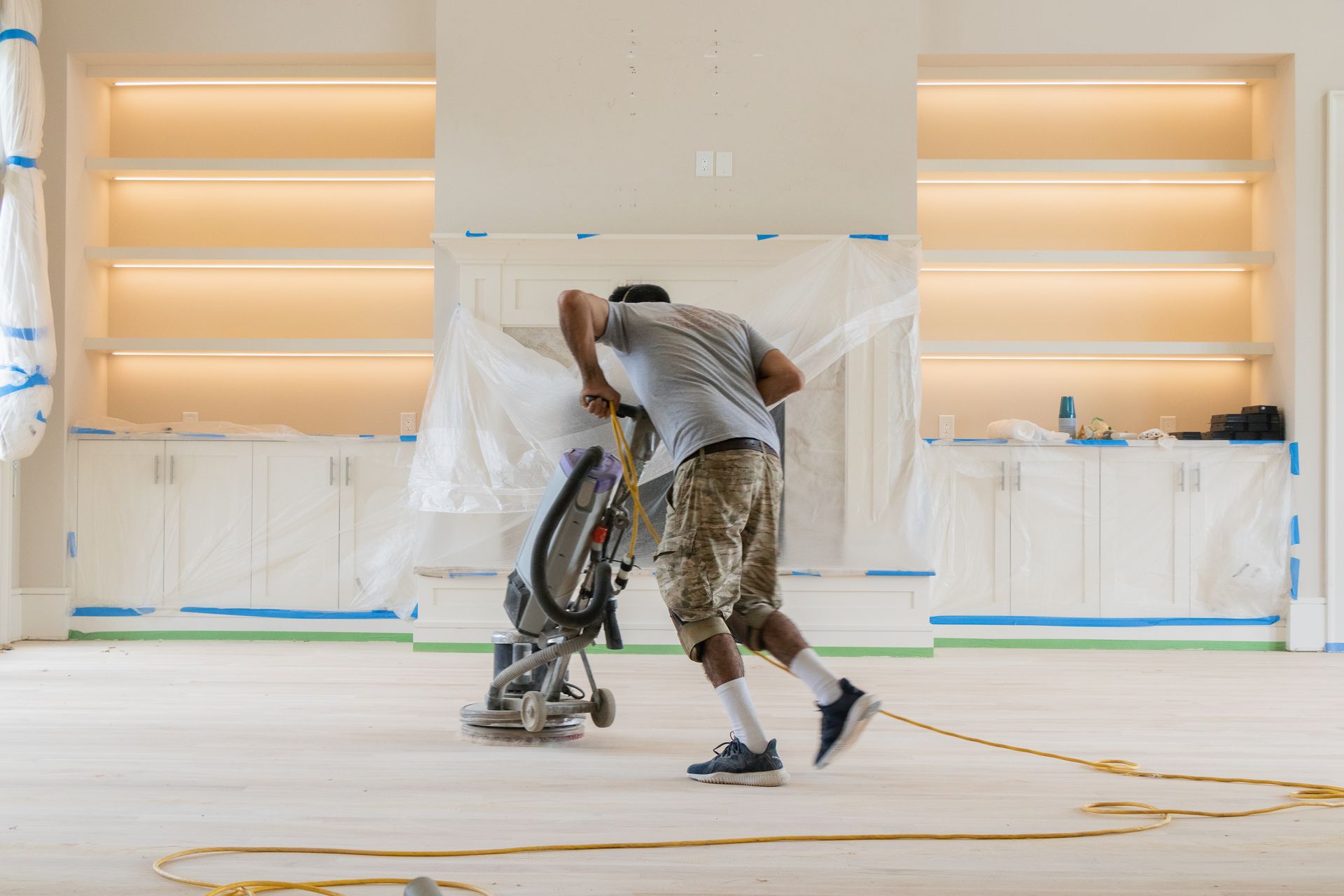 A man is using a machine to sand the floor of a room.