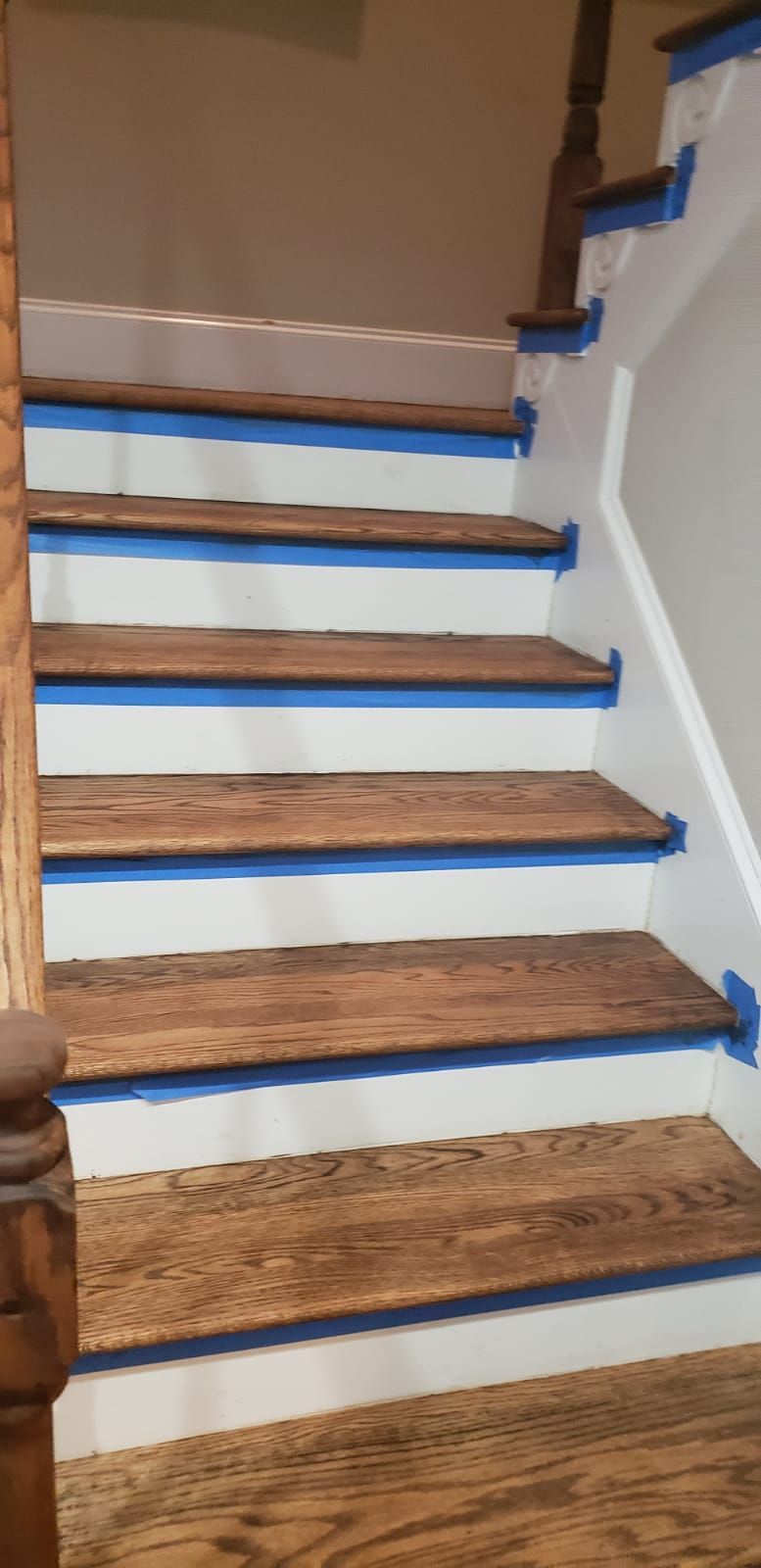 A wooden staircase with white steps and blue tape on the steps.