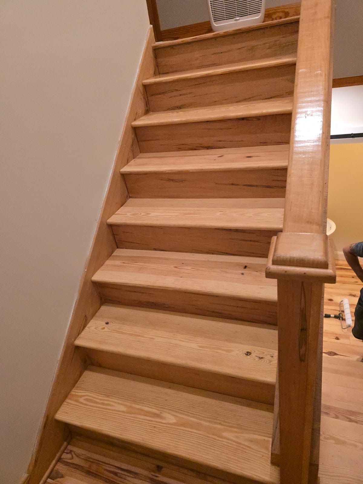 A person is standing next to a wooden staircase in a room.