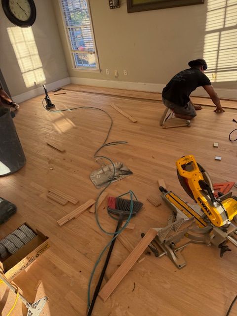A man is working on a wooden floor in a living room