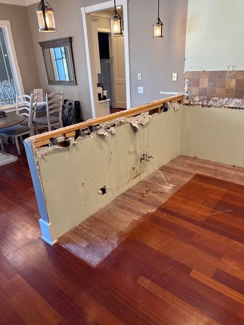 A kitchen with a wooden floor and a broken wall.