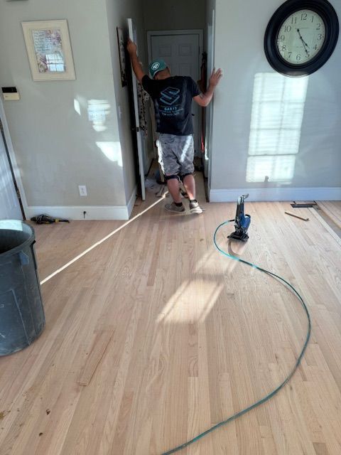 A man is standing on a wooden floor in a living room next to a clock.