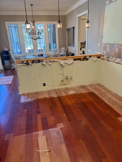 A kitchen with hardwood floors and a broken wall.