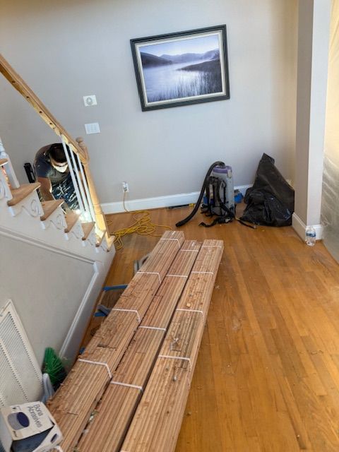 A stack of wood is sitting on the floor in a room next to a staircase.