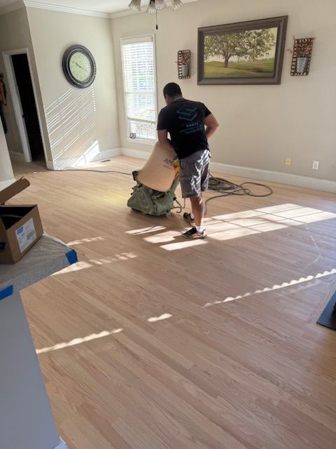 A man is sanding a wooden floor in a living room