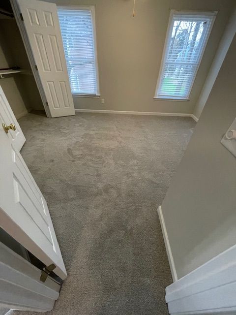 An empty bedroom with a carpeted floor and two windows.