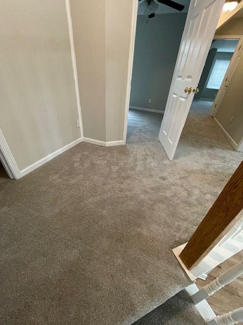 A hallway with a carpeted floor and stairs in a house.