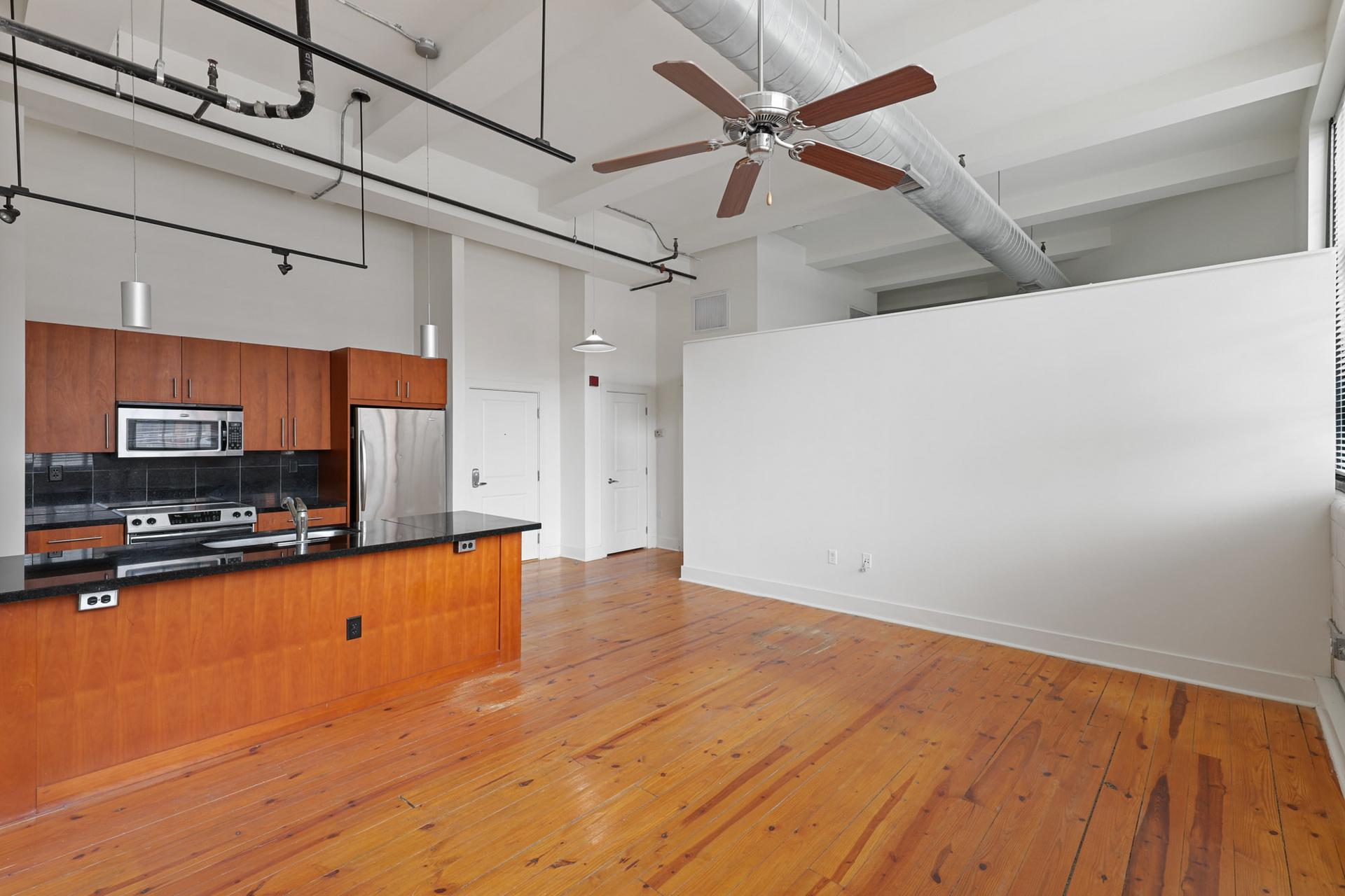 An empty kitchen with wooden floors and a ceiling fan.