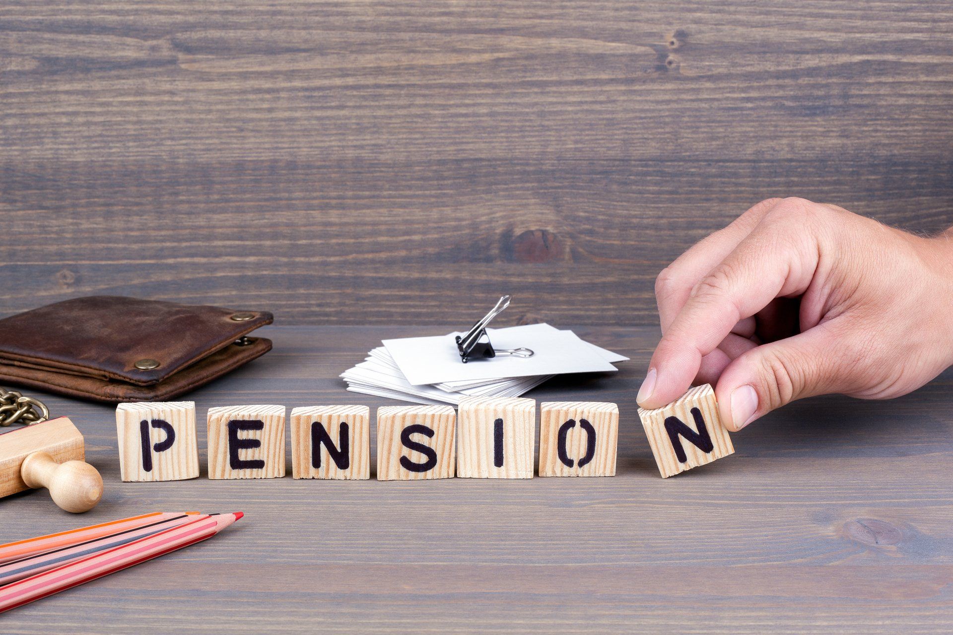 A person is arranging wooden blocks to spell the word pension.