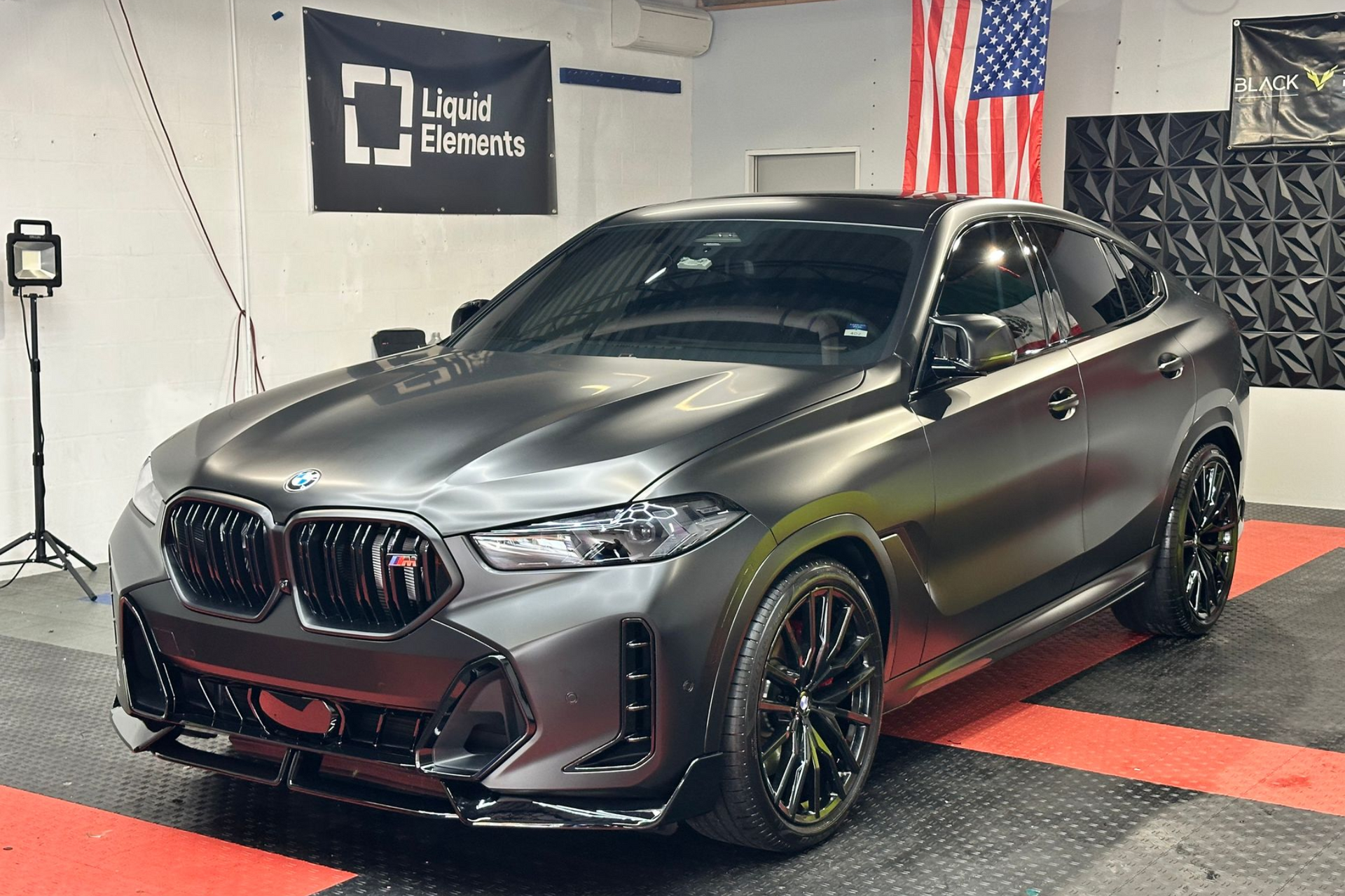 Black Lexus GX in a garage, reflecting the overhead lights. American flag in the background.