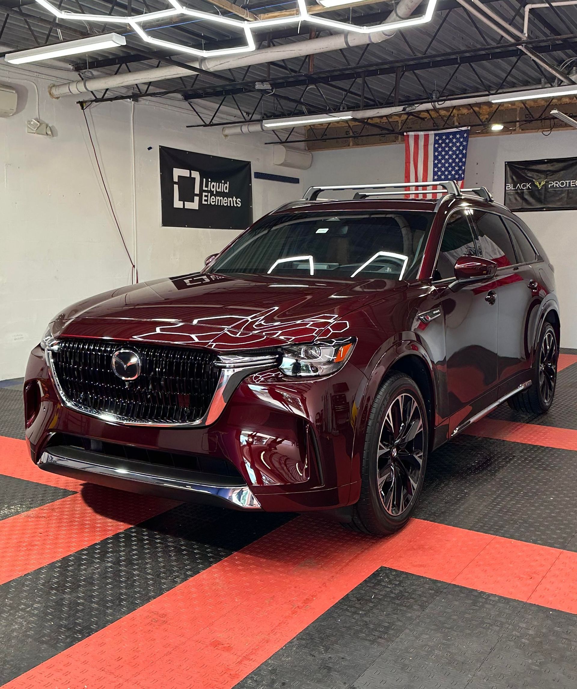 Maroon Mazda CX-90 SUV in a garage with American flag and black rims.