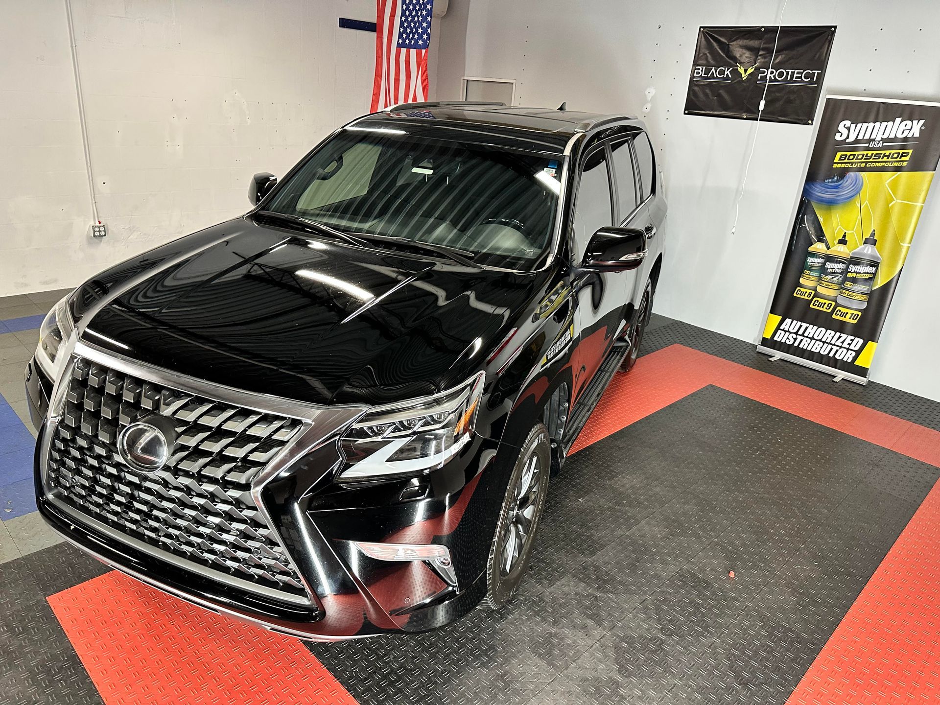 Black Lexus GX in a garage, reflecting the overhead lights. American flag in the background.