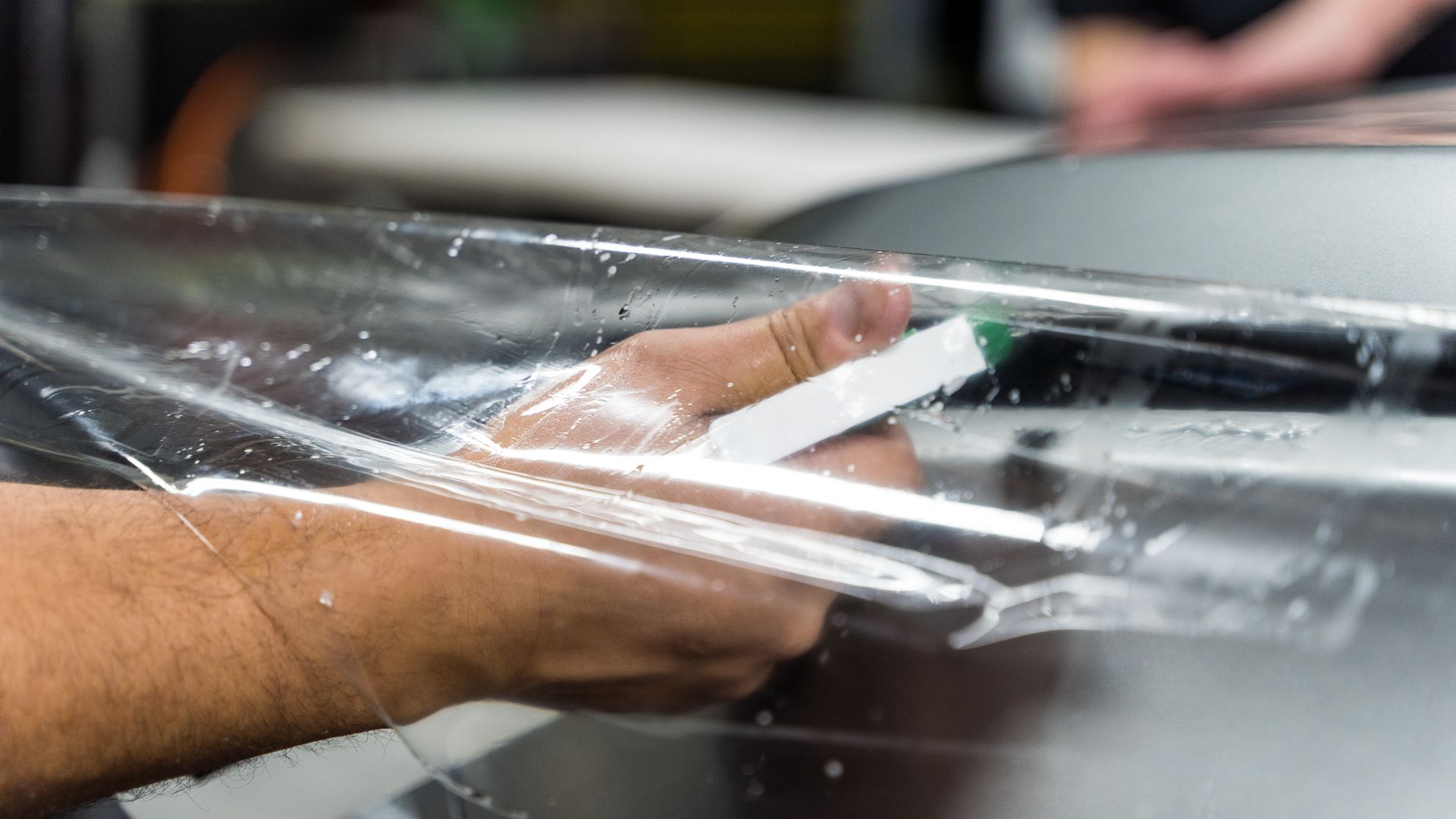 A person applying clear protective film to a car's surface, using a squeegee tool.