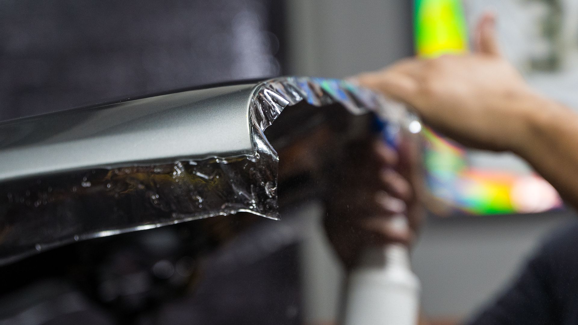Person applying car wrap, black film being smoothed onto the silver car panel.