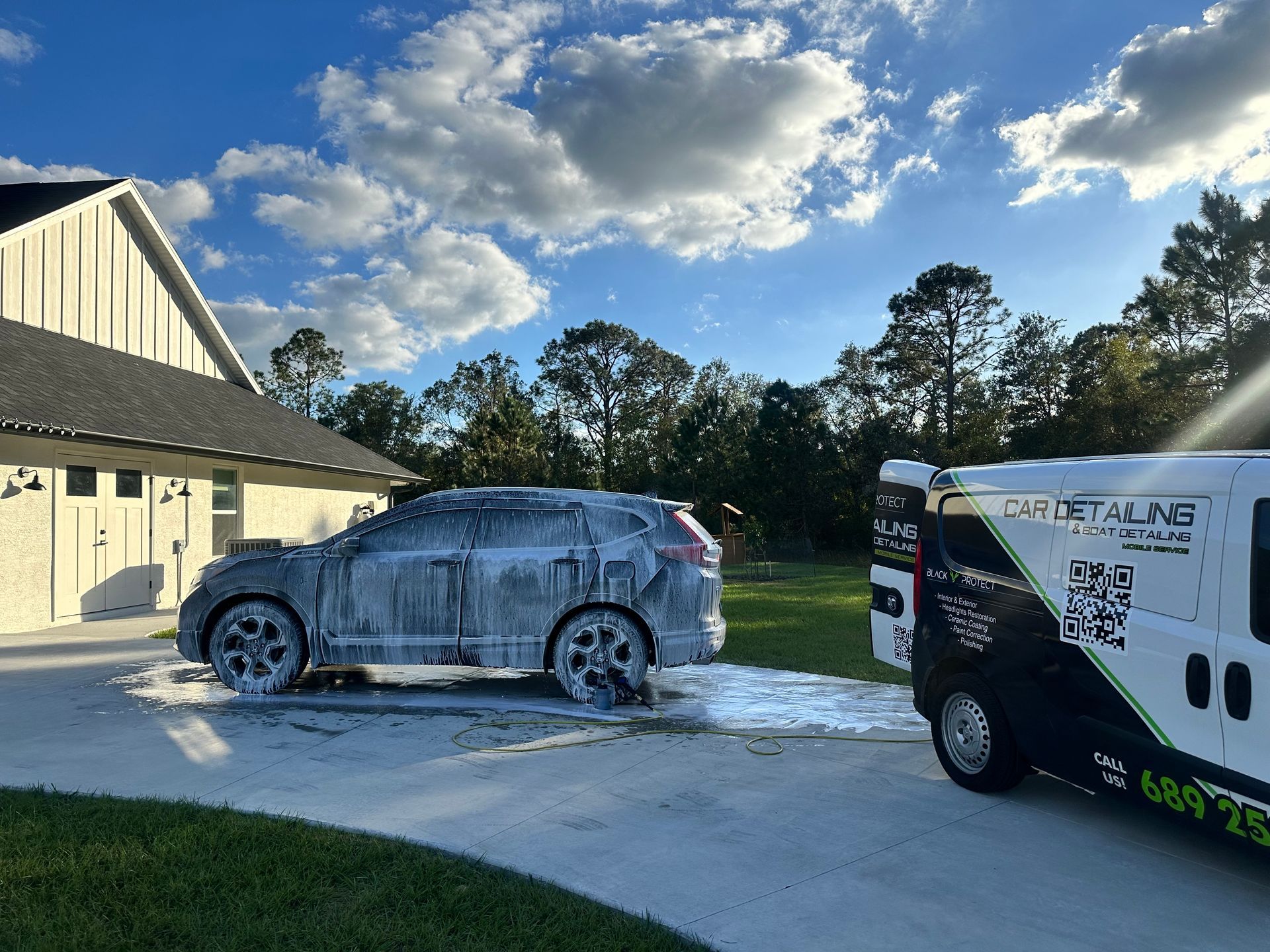 A white car is parked in front of a house next to a van.